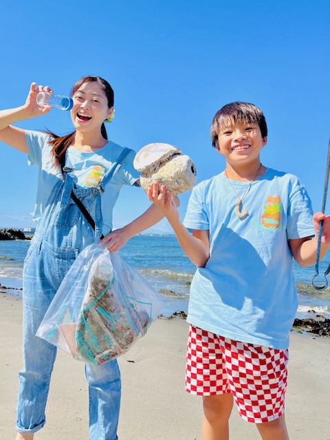 青空のもと、砂浜で拾ったごみを手にしている女性と男児の写真