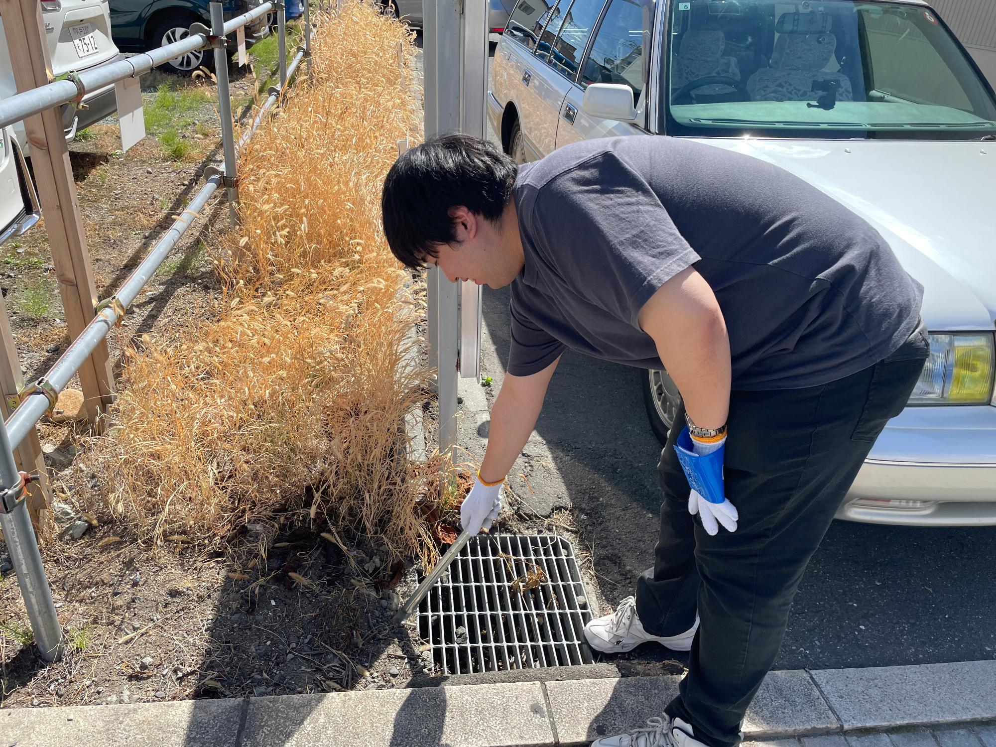 駐車場の周りのごみをトングで拾っている男性の写真