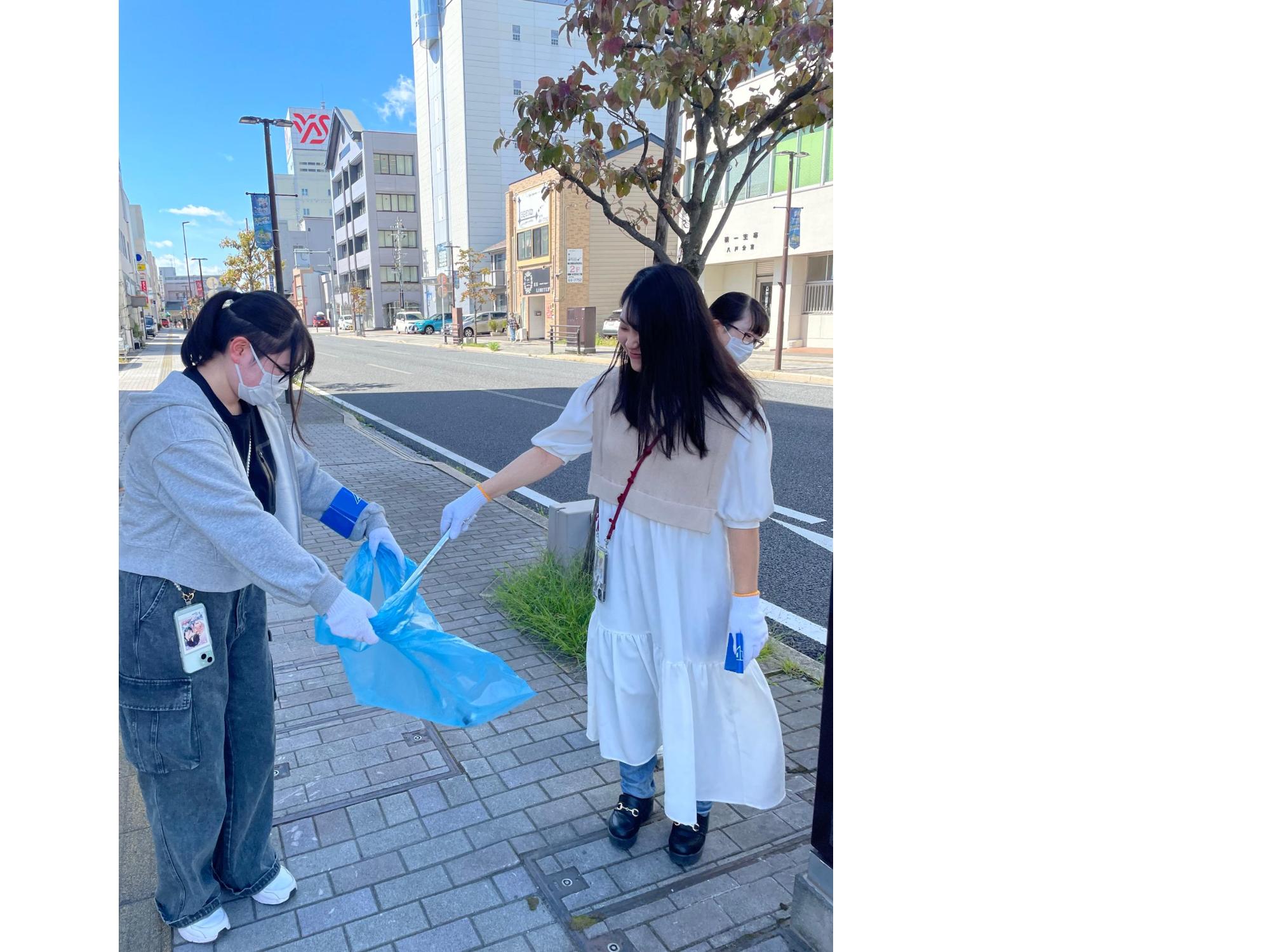 中心街の歩道のごみをトングで掴んで、もう一人の持つ袋に入れている女性二人の写真