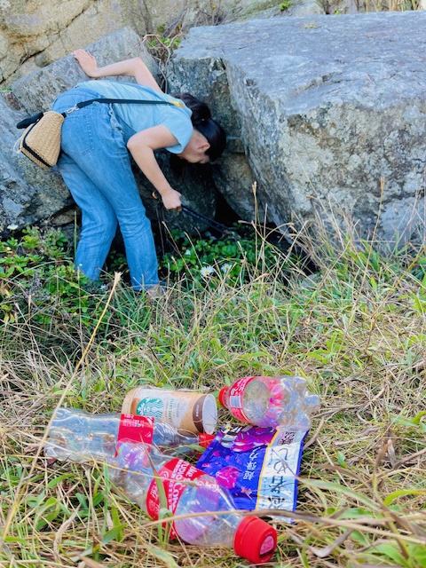 大きな岩の間のごみをトングで集めている女性と、回収したペットボトル等のごみの写真