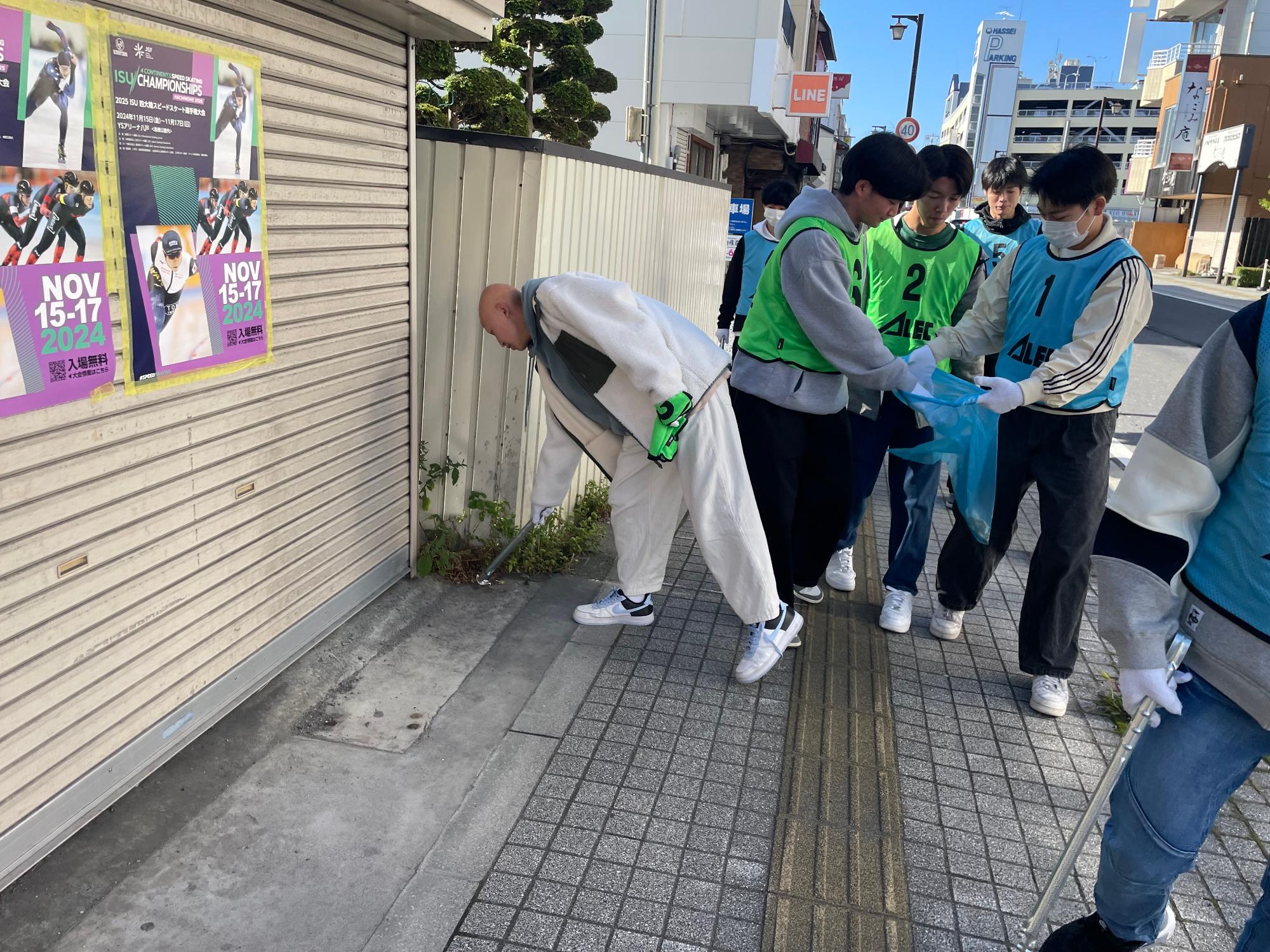 中心街の歩道のごみを拾うアレックのビブスを着用した参加者の写真