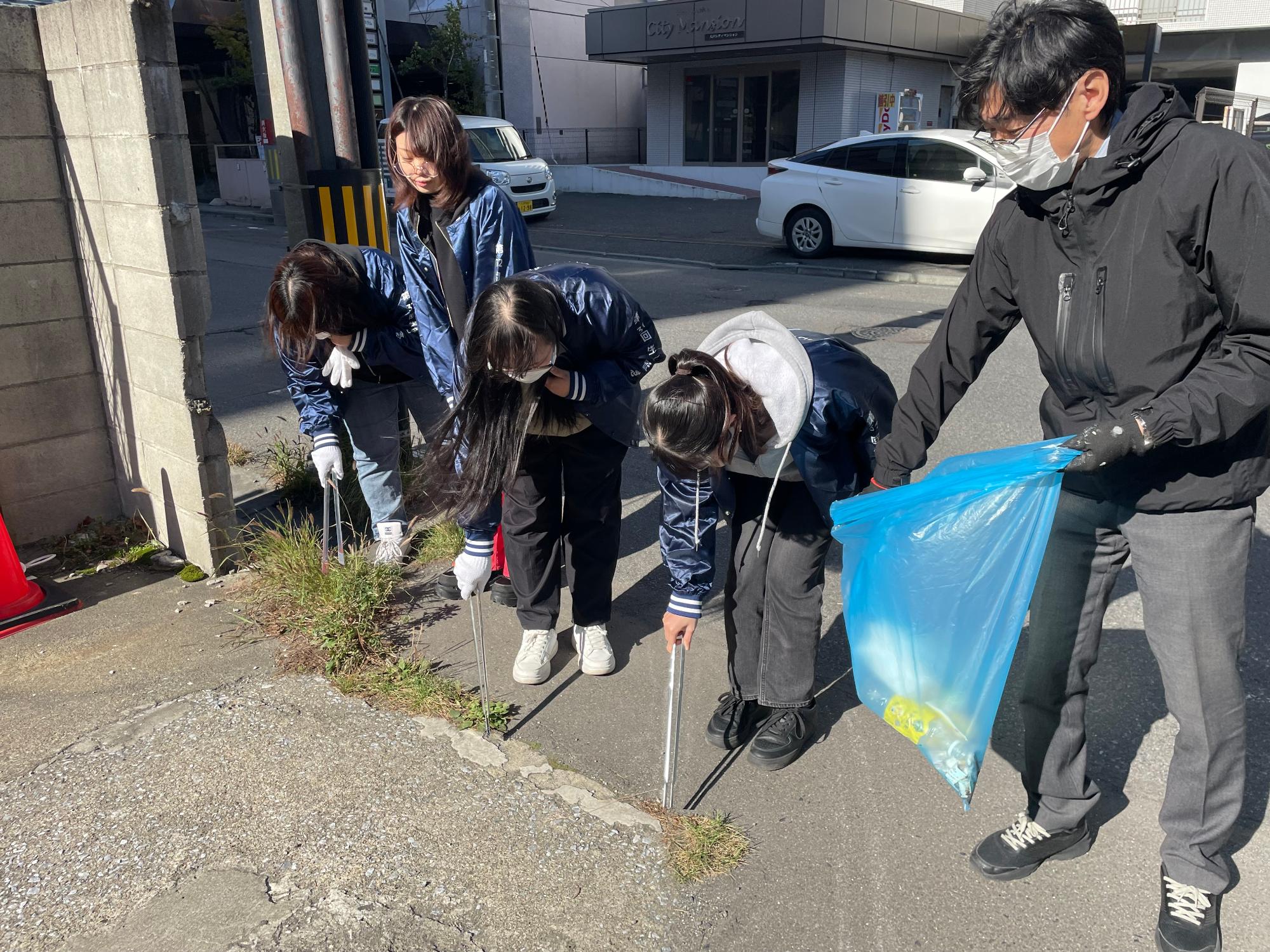 道路の草の生えている場所のごみを拾う参加者の写真