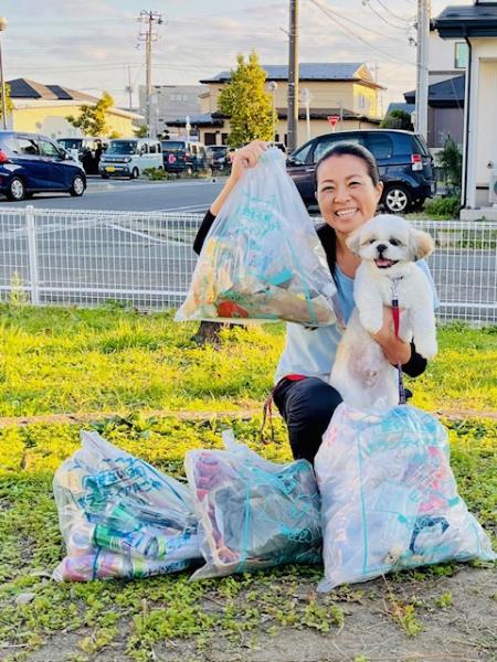 集めたごみと、かわいい白い犬を小脇に抱えた女性の写真。