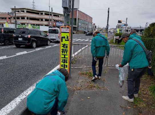 同じジャンパーで車通りの多い道路脇の歩道のごみを集めている参加者3人の写真。