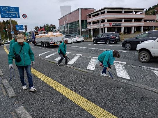 根城の車が多く走行している大きな道路。車の見える歩道でごみをトングで拾っている参加者3人の写真。