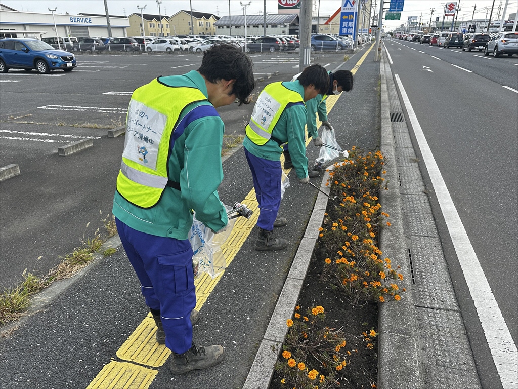 歩道にある花の植えられている場所のごみを拾っている参加者3名の写真。クリーンパートナーのビブスを着用している。