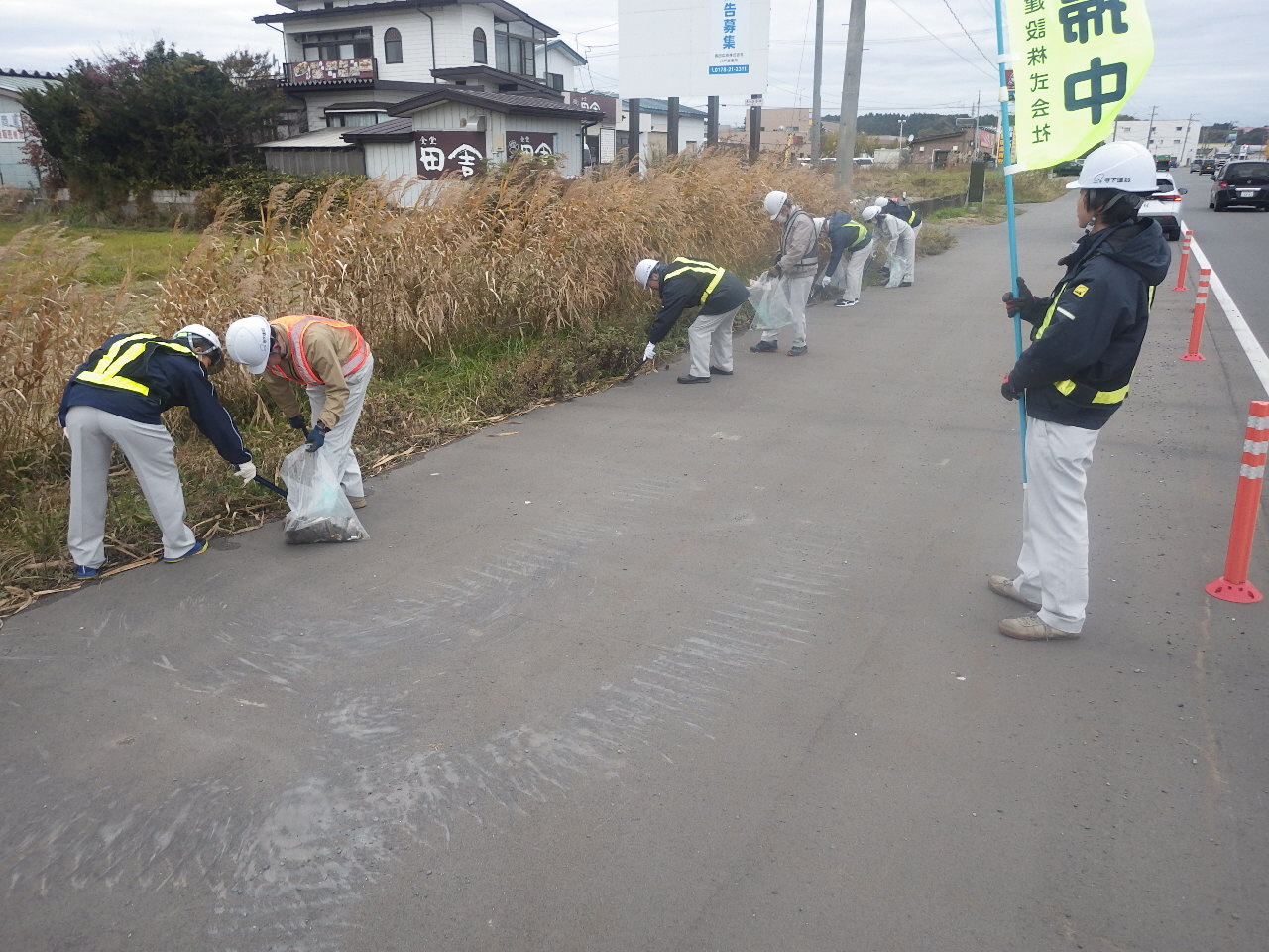 長苗代の歩道と草地の間のごみを、のぼり旗を掲げて集めている参加者の写真。