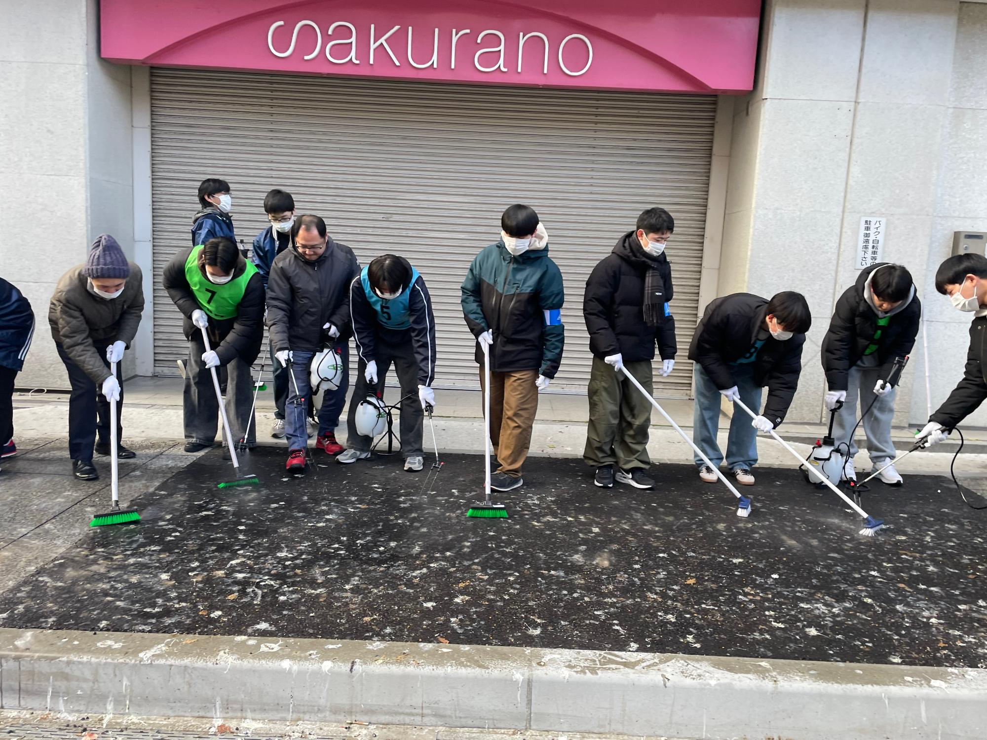歩道の鳥のフンをデッキブラシで洗い流している参加者の写真。