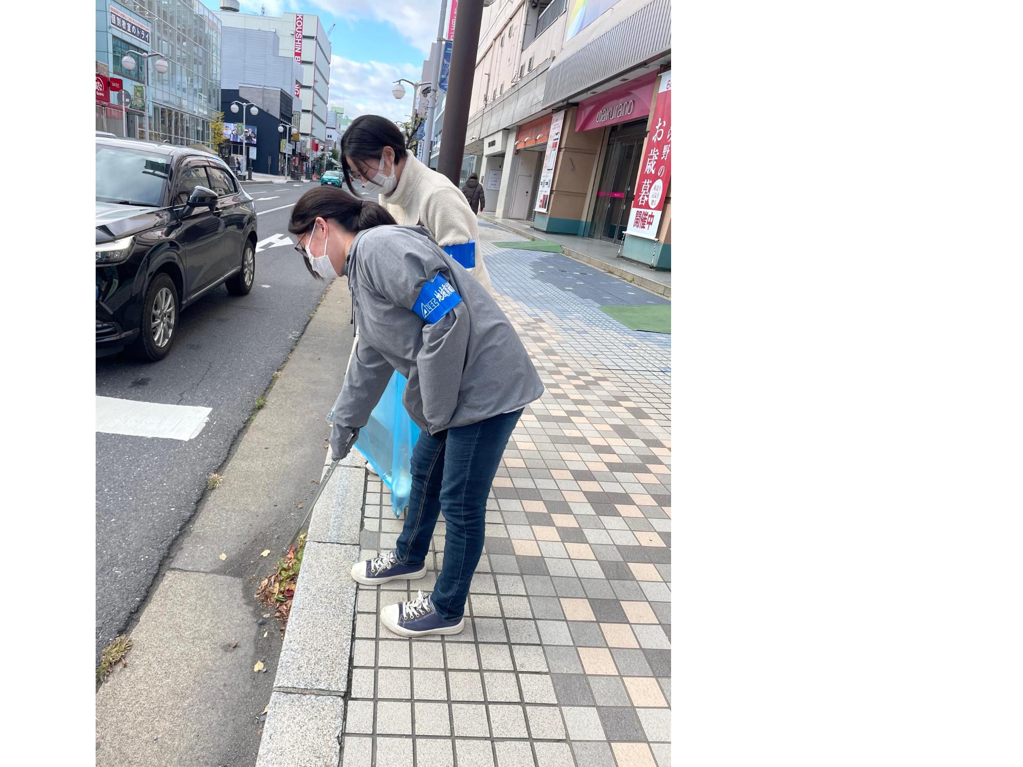 車道と歩道の隙間のごみをトングで拾っている、腕章をつけた参加者二人の写真。