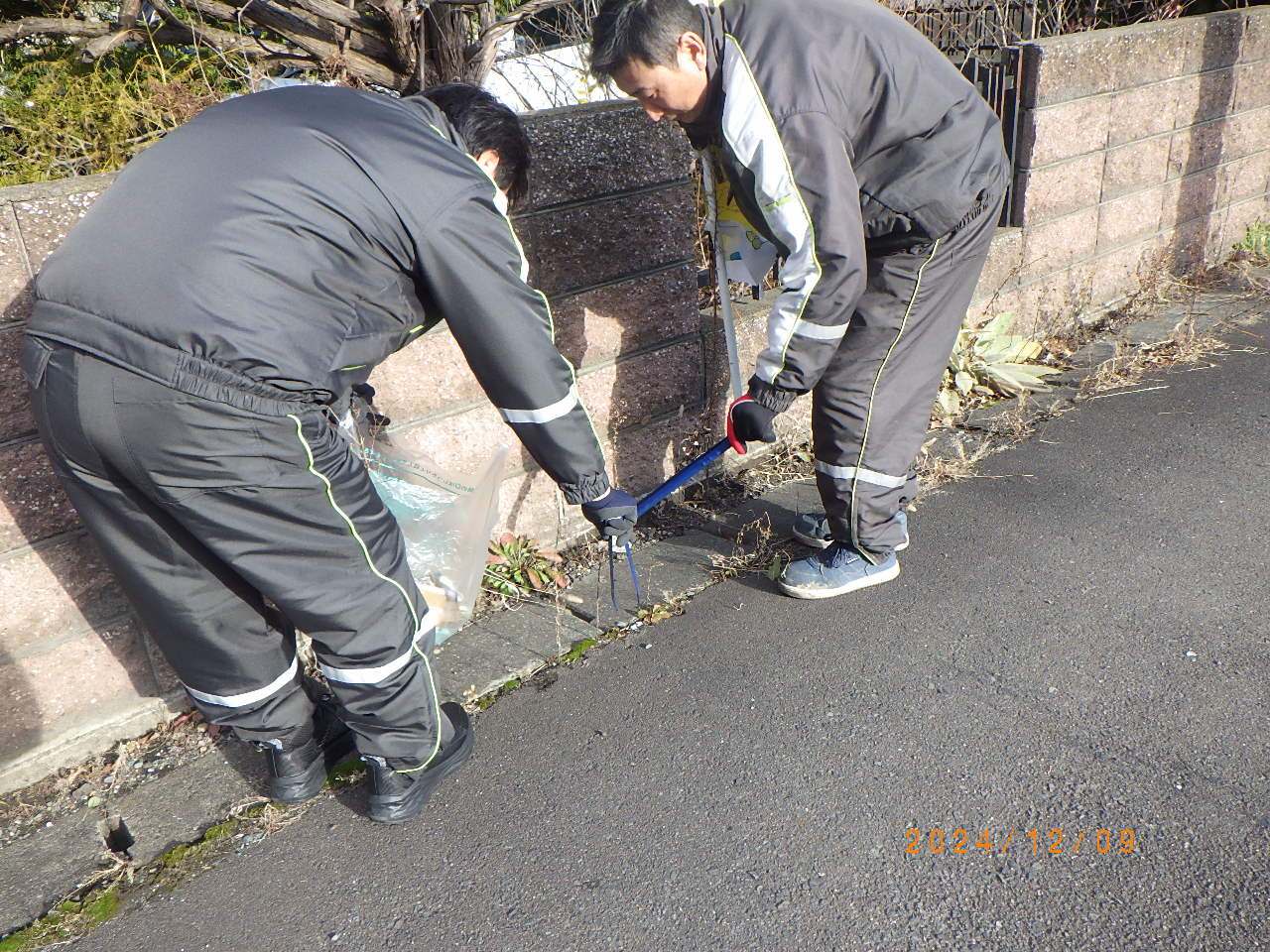 道路のごみをトングで拾ってる男性二人の写真。