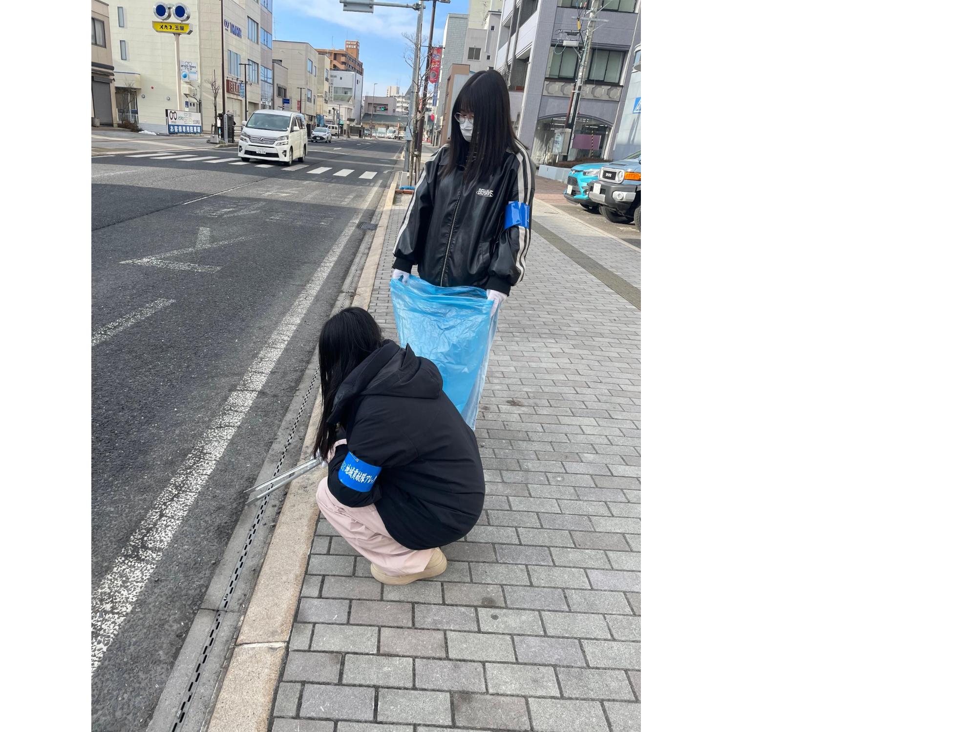 車道と歩道の間のごみをトングで拾っている女性二人の写真