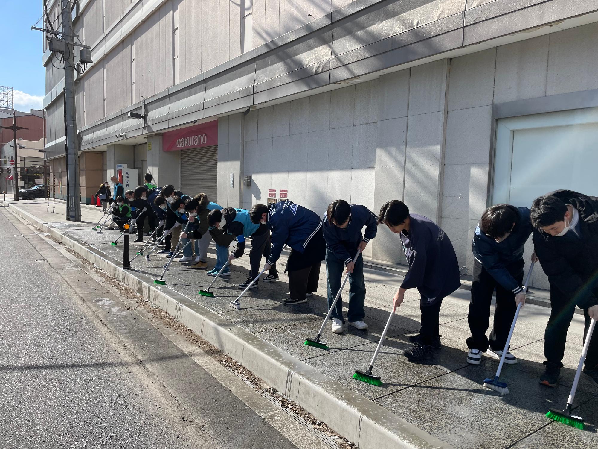 番町の歩道の鳥のフンをデッキブラシで掃除する参加者の写真。