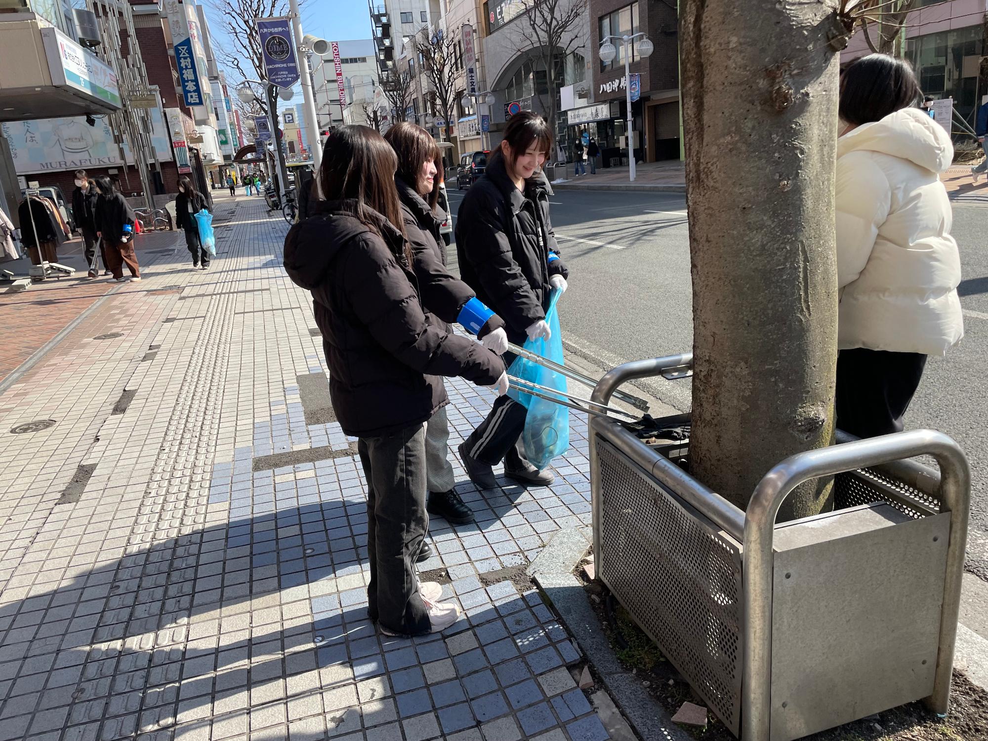 中心街の歩道のごみをトングで集めている女性参加者の写真。