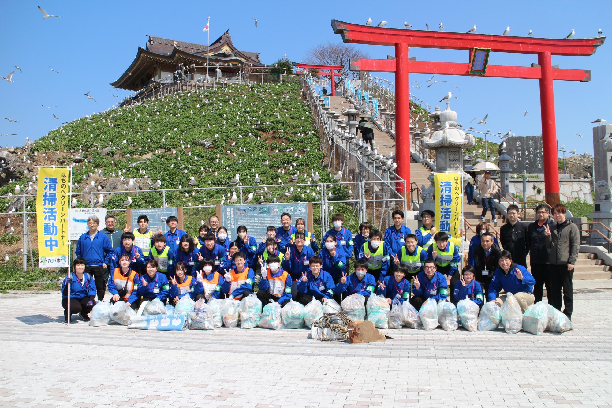 蕪島をバックに活動終了後の約60人の集合写真