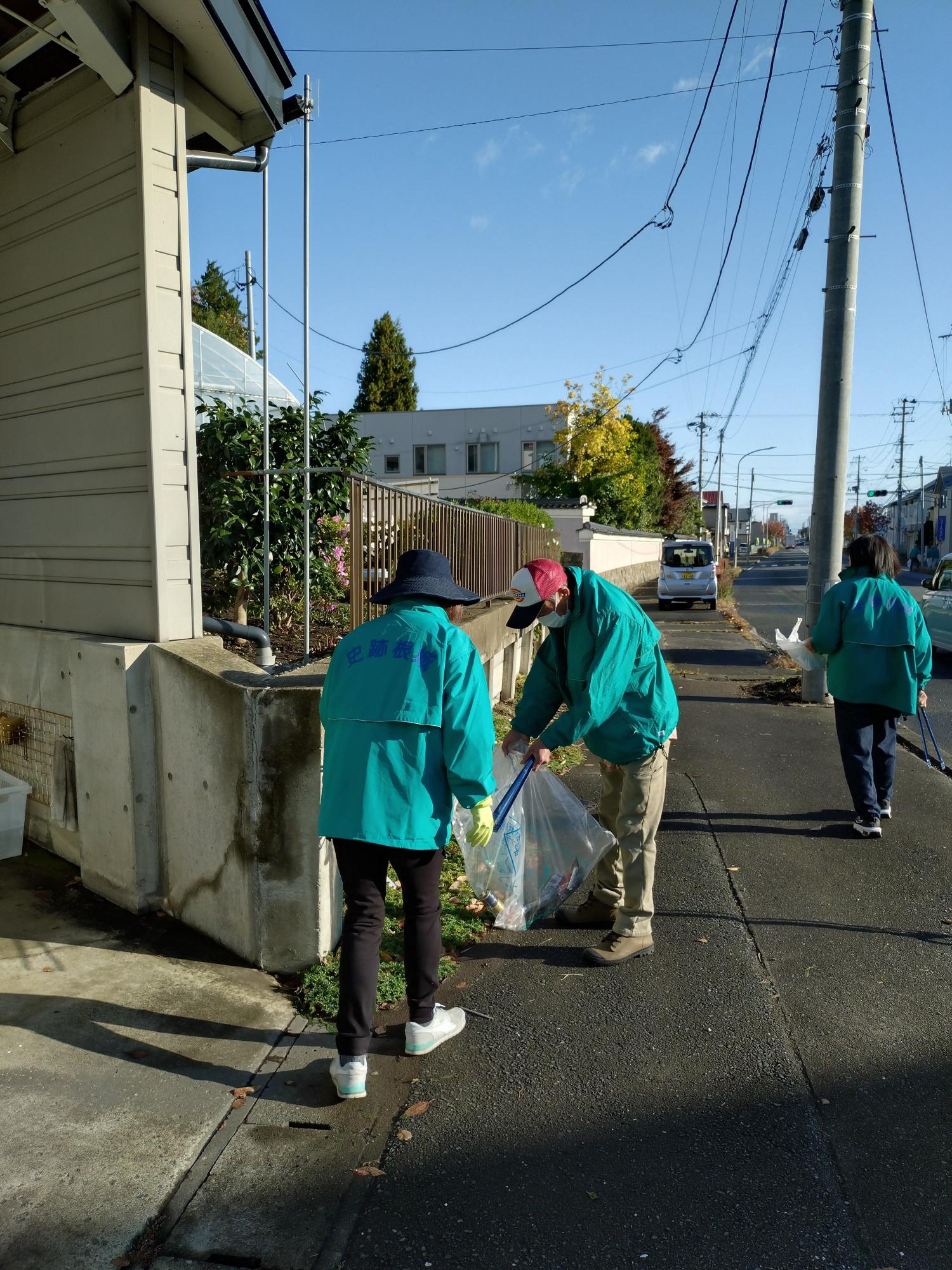 道路脇の歩道のごみを集めている参加者3人の写真。