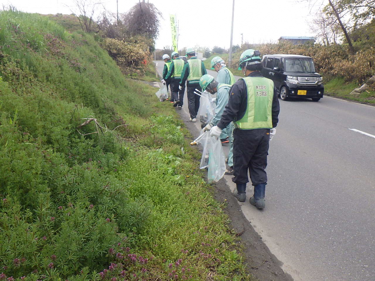 道路脇の草地のごみを拾う写真