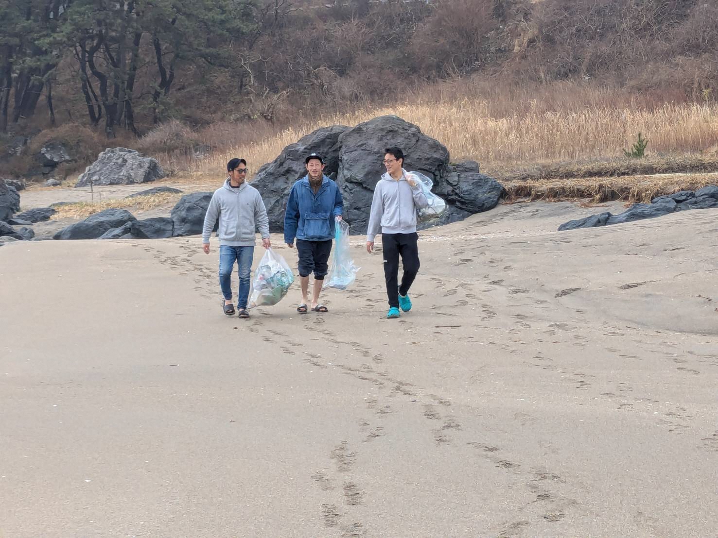 砂浜をごみ袋を持って歩いている様子