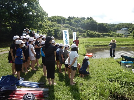 講師がため池に入り、こども達の前でたも網の使い方を実演している様子の写真