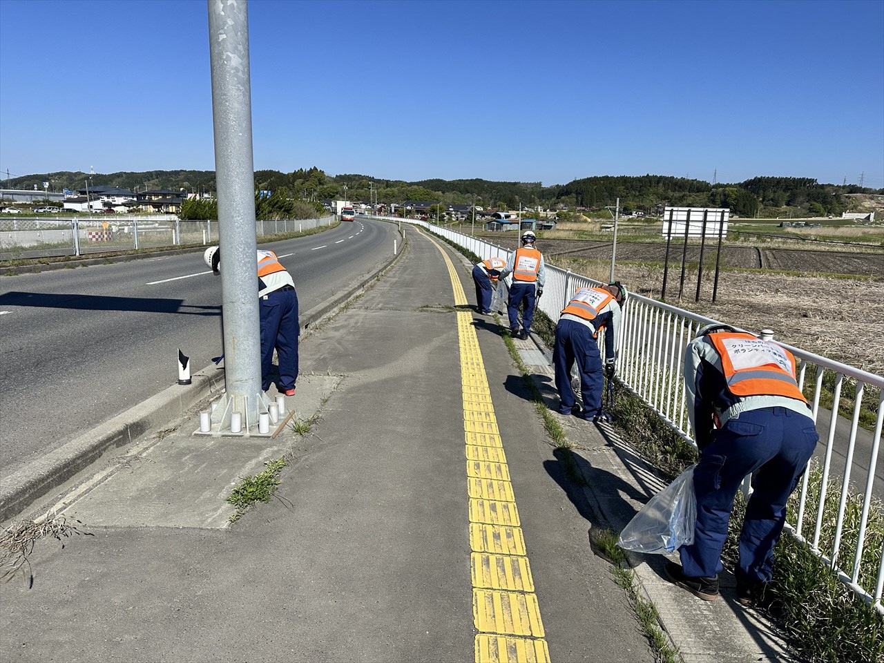 お天気の良い中歩道のごみを拾っている五人の写真 作業服にクリーンパートナーのビブスを着用している