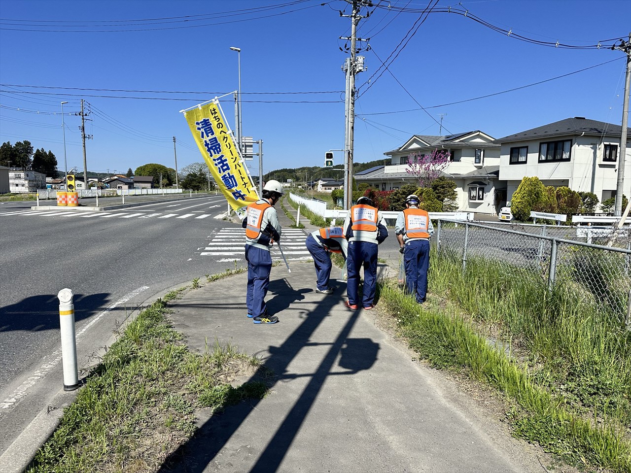 のぼり旗を掲げて交差点付近のごみを拾う人たちの写真