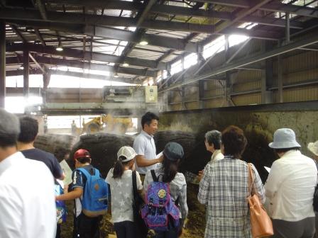 施設内に広げられ置かれた堆肥から蒸気が上がっているのを見学している参加者たちの写真