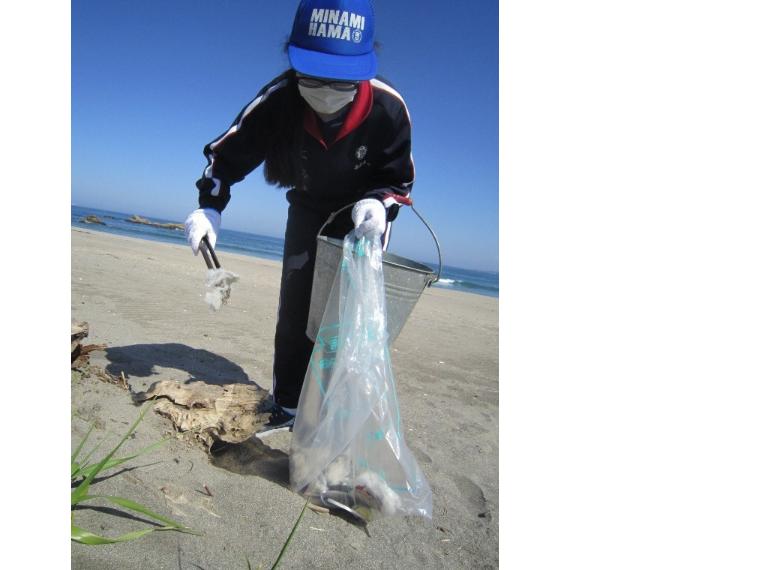 砂浜でバケツとごみ袋を左手に持ち、右手のトングでごみを集める中学生