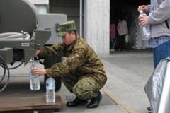 給水車から水を座ってペットボトルに入れている自衛官の写真