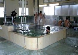 入浴施設にて湯舟に入浴している人や座って体を洗っている人たちの写真