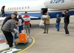 奥に飛行機、手前に荷物を確認している人や荷物を抱えた人たちの写真