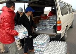 トラックバンに積まれた500ミリリットルの水を運び出している人たちの写真