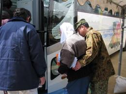 左にバス、バスに乗ろうとしている人に手を添えて乗り込む手伝いをしている自衛隊員の写真
