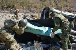 瓦礫となった薄緑のトタンを持ち上げようとしている自衛隊員2名の写真