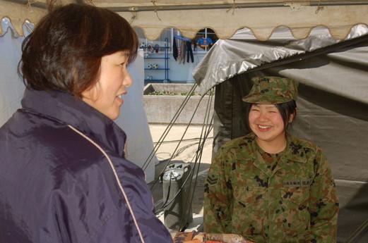 屋外テントにて左に立つ女性と笑顔で話をしている女性自衛隊員の写真