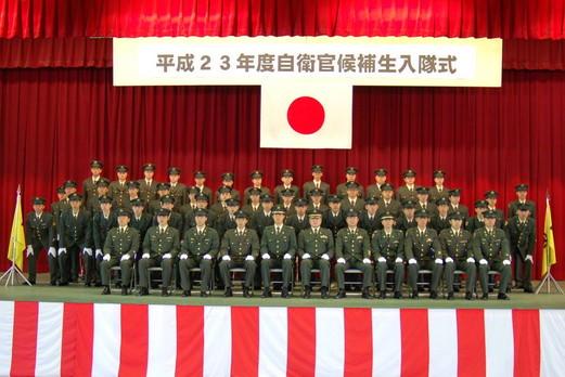 室内にて平成23年度自衛官候補生入隊式の垂れ幕、日本国旗の前で3列に整列して記念撮影をしている制服姿の人たちの写真