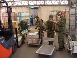 左にフォークリフト、台車を使って物資を積み込む自衛隊員たちの写真