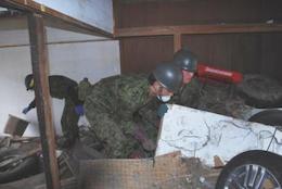 瓦礫が積もった家屋の中を捜索する自衛隊員3名の写真