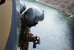 ヘリコプターから乗り出して川を捜索しているヘルメットをかぶった自衛隊員の写真