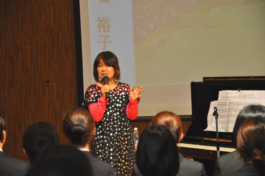ピアノの前に立ってマイクを使って話をしている豊嶋さんの写真