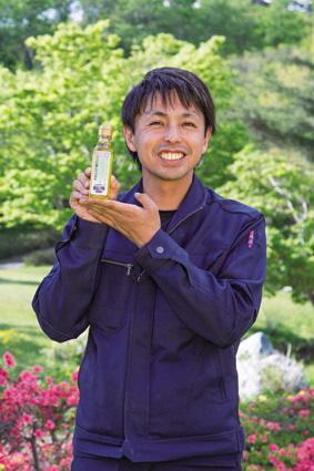 小さなボトルを掲げ、笑顔の沢森 靖史さんの写真