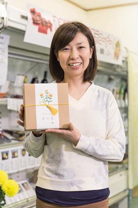 小さな箱に梱包された食用菊を掲げて笑顔で写る 岩城 美果さんの写真
