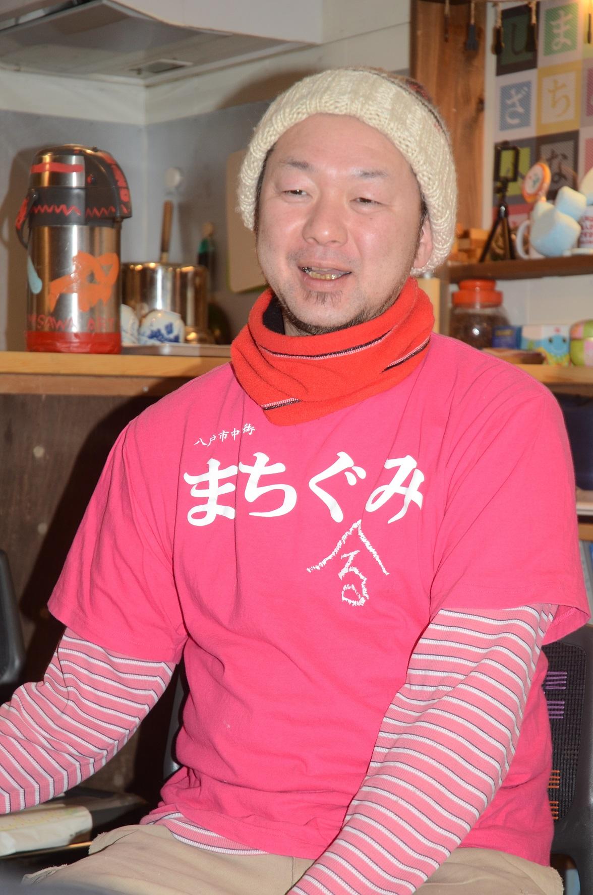 ベージュのニット帽をかぶり、「まちぐみ」のピンクのTシャツを着た山本耕一郎さんの写真