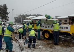 トラックに瓦礫を積み込む人たちの手前で掃除をしている作業員の写真
