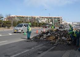 左に乗用車、右に道の端に寄せられた瓦礫を警備している作業員の写真