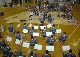 体育館の床に座っている観客を前に大湊音楽隊の演奏している様子を上から撮影した写真