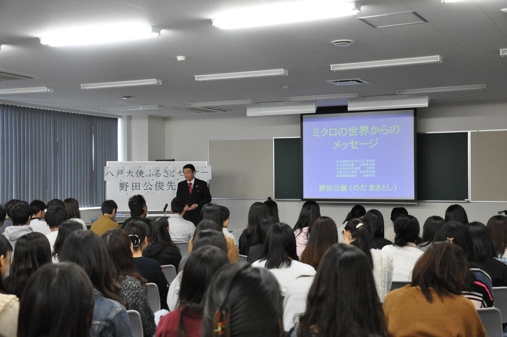 前に立って話をしている野田先生と席に着いている学生たちを、教室後方から撮影した写真