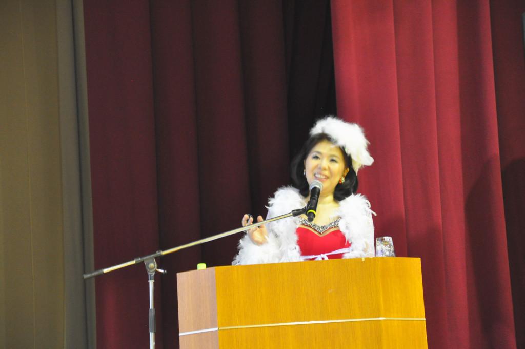 演台の前に立つ、赤と白の衣装を身に着けた吉岡さんの写真