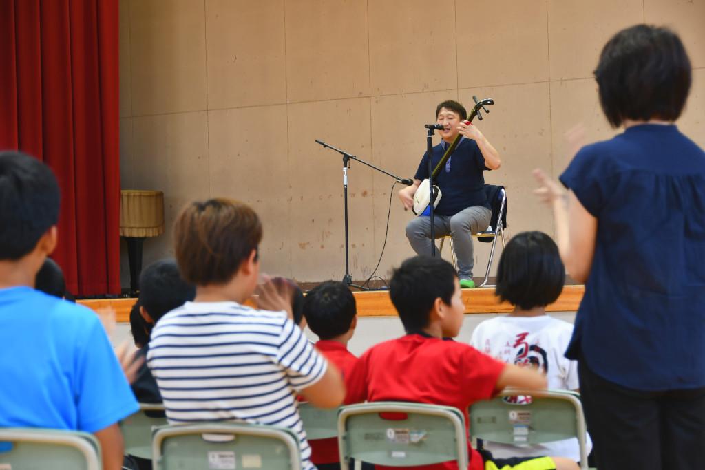 ステージ上で三味線の演奏を披露する松田さんに拍手を送る生徒たちの写真