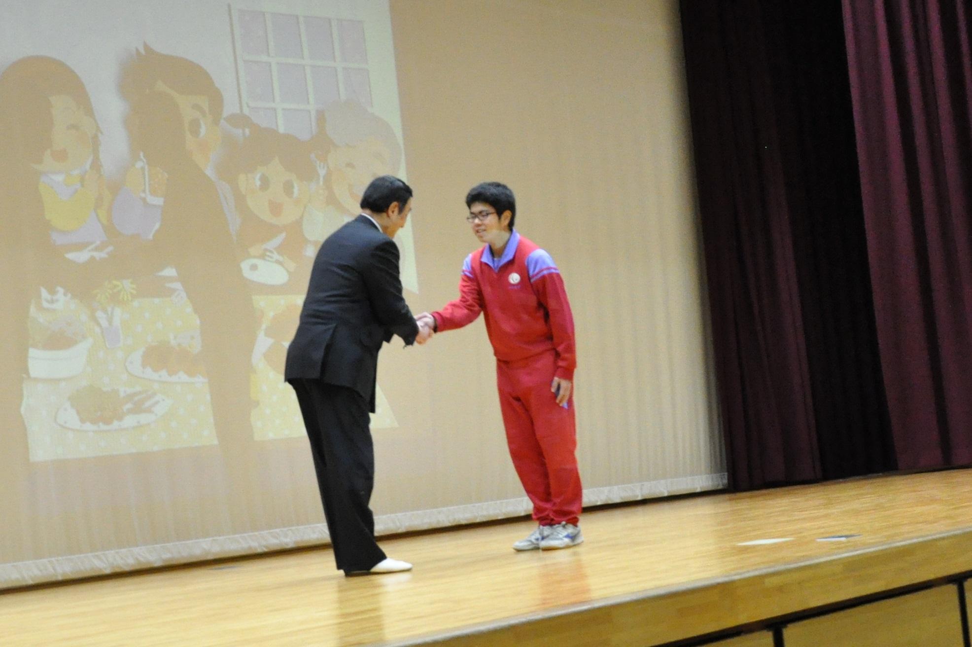 舞台の上で握手をしている代表生徒と野田先生の写真