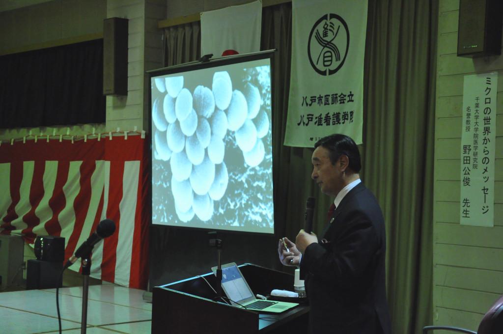 スクリーン横で話をしている野田先生の写真