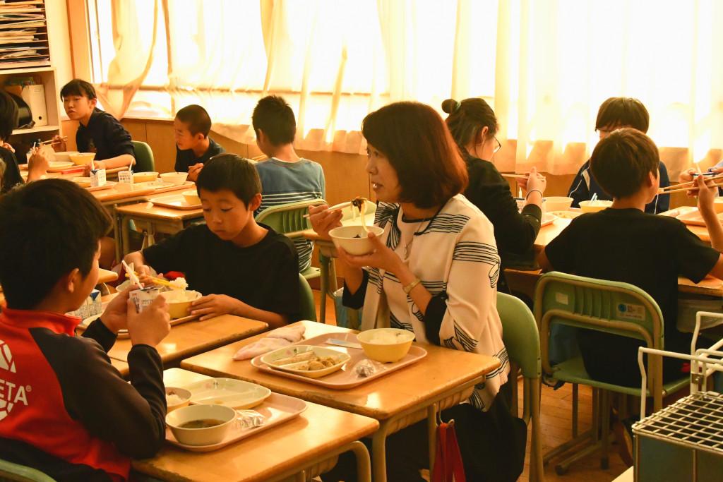 教室で生徒たちと一緒に給食を食べる梅内さんの写真